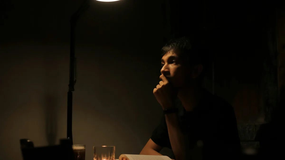 Une personne assise seule &agrave; une table dans une pi&egrave;ce sombre
