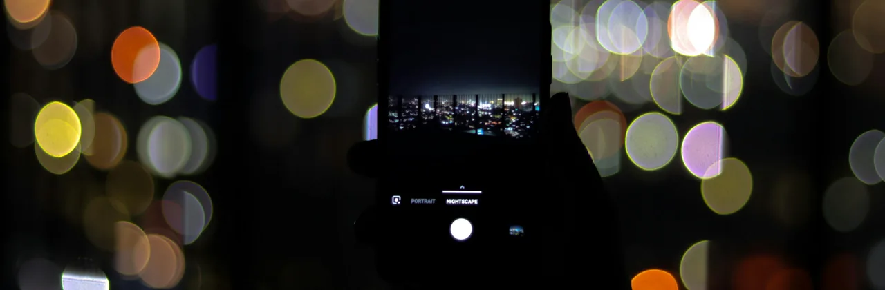 Un t&eacute;l&eacute;phone tenu &agrave; bout de bras la nuit devant des lumi&egrave;res color&eacute;es